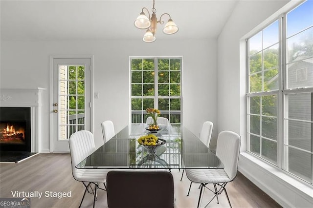 dining room with wood finished floors, healthy amount of natural light, a lit fireplace, and a chandelier