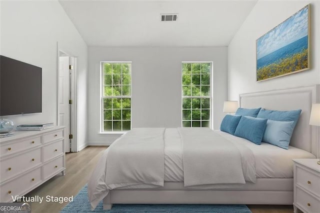 bedroom with vaulted ceiling, multiple windows, and light wood-type flooring