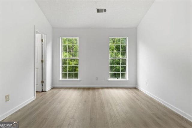 spare room with wood finished floors, baseboards, and plenty of natural light