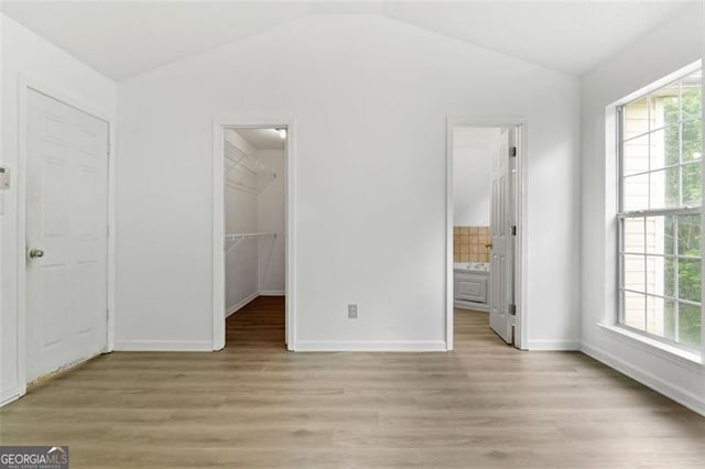 unfurnished bedroom with lofted ceiling, light wood-style flooring, a spacious closet, baseboards, and ensuite bath