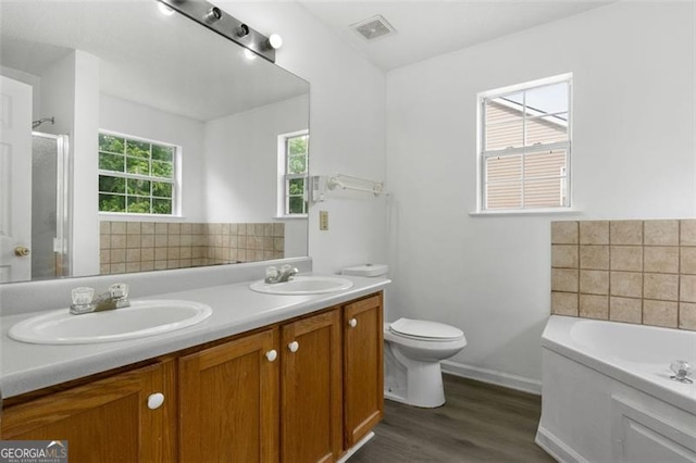 bathroom with wood finished floors, a bath, baseboards, toilet, and double vanity