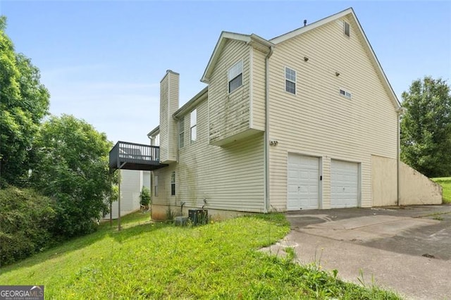 view of side of property with an attached garage, concrete driveway, a chimney, and a yard