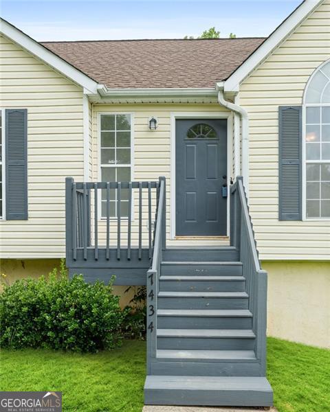 view of exterior entry featuring roof with shingles and a yard