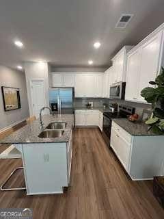 4261 Notting Hill Dr SW, Atlanta, GA 30331 - kitchen featuring stainless steel appliances, dark wood finished floors, a kitchen island with sink, white cabinetry, and a breakfast bar area