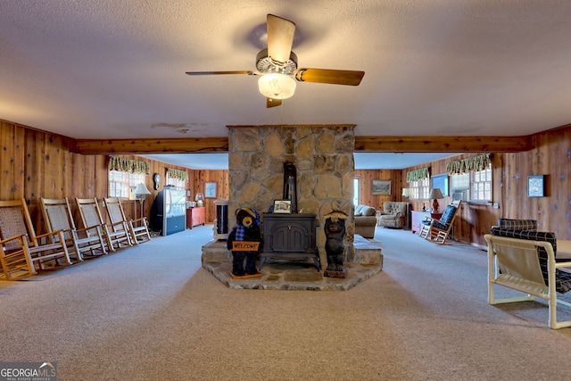 carpeted living area featuring wooden walls, a wood stove, a textured ceiling, and a ceiling fan