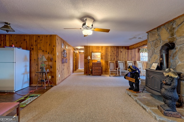 living area with a wood stove, wood walls, ceiling fan, a textured ceiling, and carpet flooring