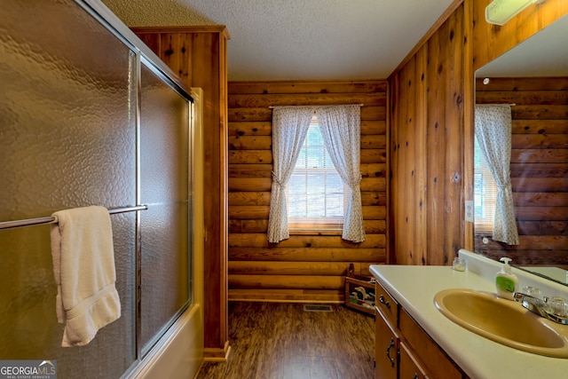 full bathroom featuring rustic walls, hardwood / wood-style flooring, a textured ceiling, vanity, and combined bath / shower with glass door
