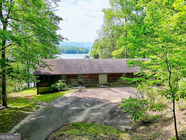 cabin featuring log exterior, driveway, a chimney, a water and mountain view, and a shingled roof