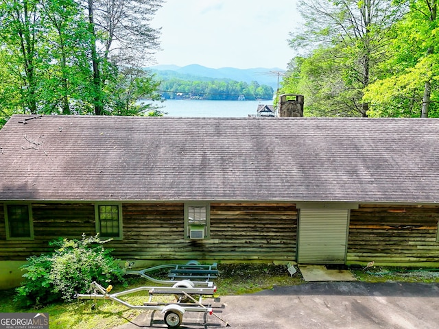 exterior view of a chimney, log siding, a water and mountain view, and a shingled roof