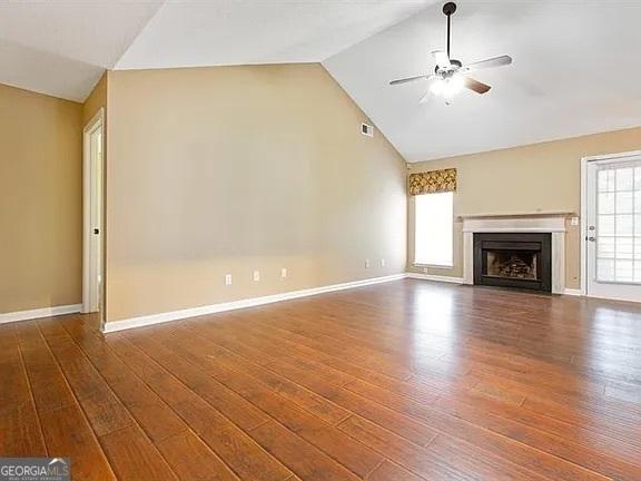 unfurnished living room with ceiling fan, wood finished floors, a fireplace with flush hearth, baseboards, and high vaulted ceiling