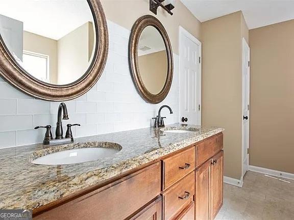 full bath with decorative backsplash, double vanity, and baseboards
