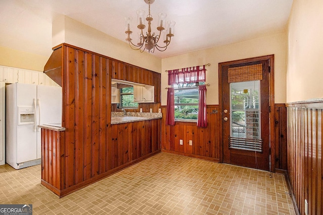 894 Nottingham Dr, Avondale Estates, GA 30002 - kitchen with white refrigerator with ice dispenser, a wainscoted wall, a chandelier, brick patterned flooring, and wood walls