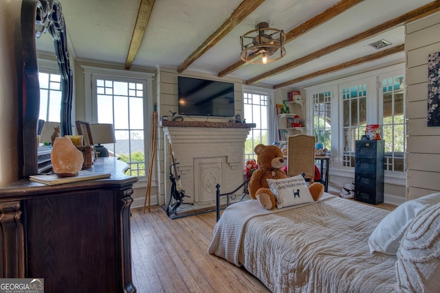 bedroom featuring beam ceiling, a fireplace, and light wood-style flooring