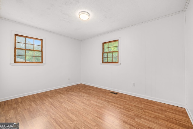 spare room with light wood-style floors, ornamental molding, baseboards, and a textured ceiling