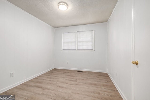 spare room with a textured ceiling, light wood finished floors, ornamental molding, and baseboards