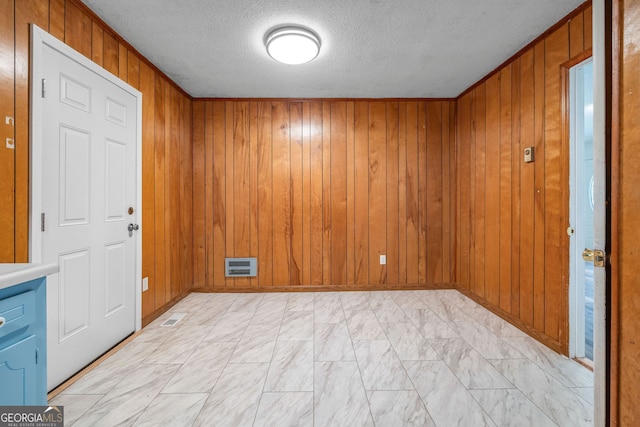 unfurnished room featuring a textured ceiling, wood walls, and light marble finish flooring