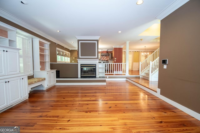 24 Overbrook Ct, Newnan, GA 30263 - unfurnished living room featuring crown molding, light wood-type flooring, stairs, a glass covered fireplace, and a chandelier