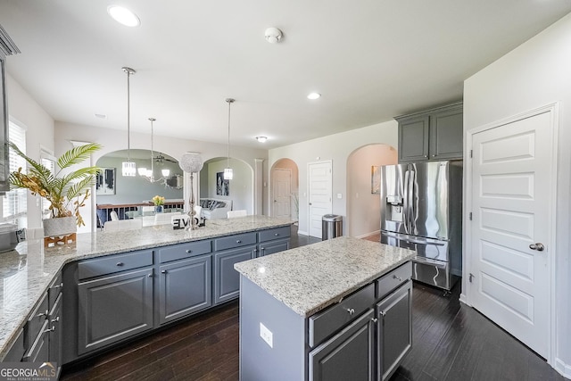 kitchen featuring stainless steel fridge with ice dispenser, arched walkways, dark wood-style floors, a chandelier, and a kitchen island