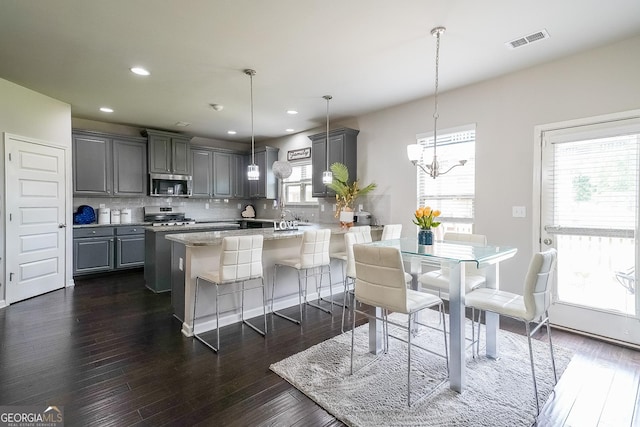 kitchen featuring stainless steel appliances, gray cabinets, decorative backsplash, a peninsula, and dark wood-style floors
