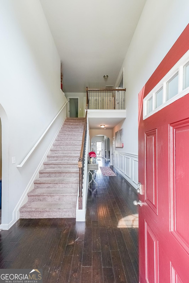 foyer entrance with arched walkways, stairs, hardwood / wood-style flooring, and a towering ceiling