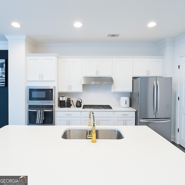 kitchen with stainless steel appliances, a sink, under cabinet range hood, crown molding, and light countertops