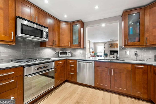 1141 Moorestown Cir, Decatur, GA 30033 - kitchen featuring appliances with stainless steel finishes, brown cabinetry, light wood-style flooring, decorative backsplash, and glass insert cabinets