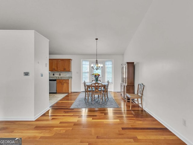 dining room with a chandelier, light wood-type flooring, baseboards, and lofted ceiling