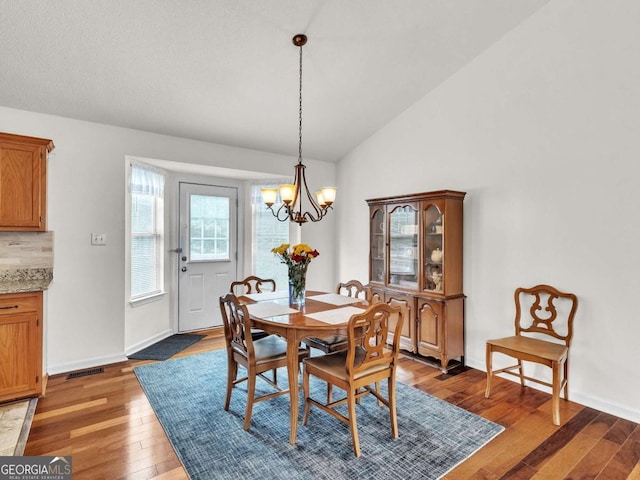 dining room featuring light wood-style floors, a chandelier, vaulted ceiling, and baseboards