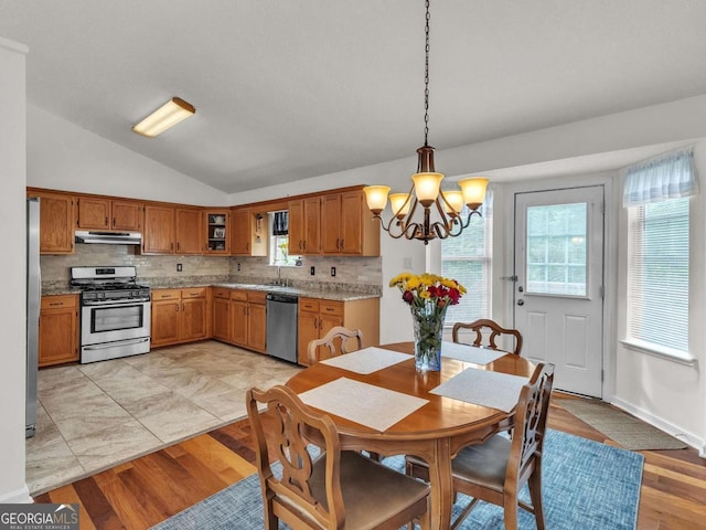 kitchen featuring stainless steel appliances, brown cabinetry, vaulted ceiling, a chandelier, and under cabinet range hood