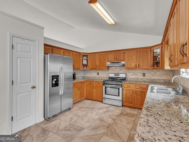kitchen with appliances with stainless steel finishes, a sink, lofted ceiling, under cabinet range hood, and brown cabinetry