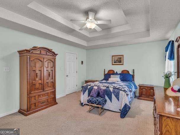 bedroom with a raised ceiling, a textured ceiling, light colored carpet, a ceiling fan, and baseboards