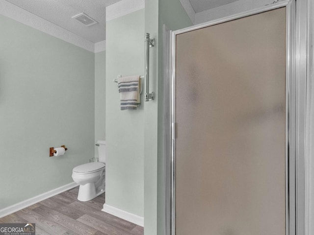 bathroom featuring a stall shower, toilet, wood finished floors, a textured ceiling, and baseboards