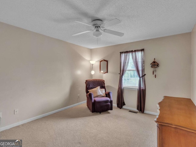 sitting room with a ceiling fan, light carpet, baseboards, and a textured ceiling