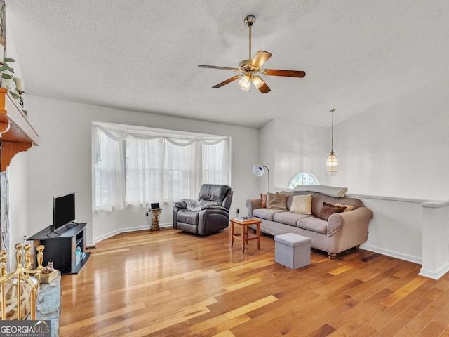 living area with ceiling fan, plenty of natural light, light wood finished floors, baseboards, and vaulted ceiling