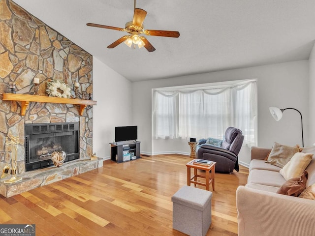 living area featuring a stone fireplace, ceiling fan, vaulted ceiling, wood finished floors, and baseboards