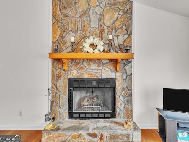 detailed view of a fireplace, wood finished floors, and baseboards