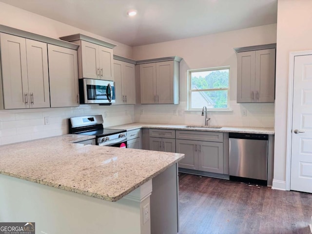 kitchen with stainless steel appliances, a sink, gray cabinets, a peninsula, and light stone counters