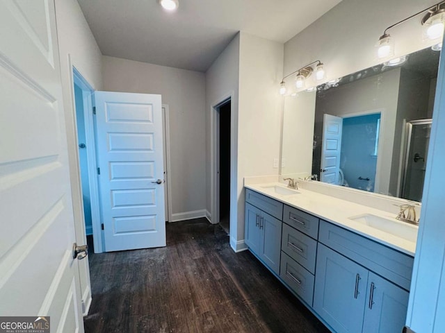 bathroom with wood finished floors, a shower stall, double vanity, and baseboards