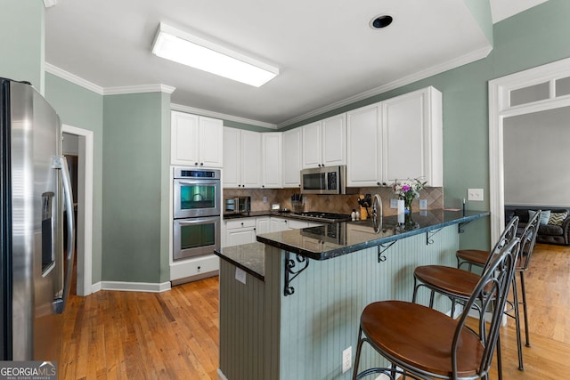 1377 Downington Ln NW, Acworth, GA 30101 - kitchen featuring appliances with stainless steel finishes, light wood-style floors, a peninsula, white cabinetry, and ornamental molding