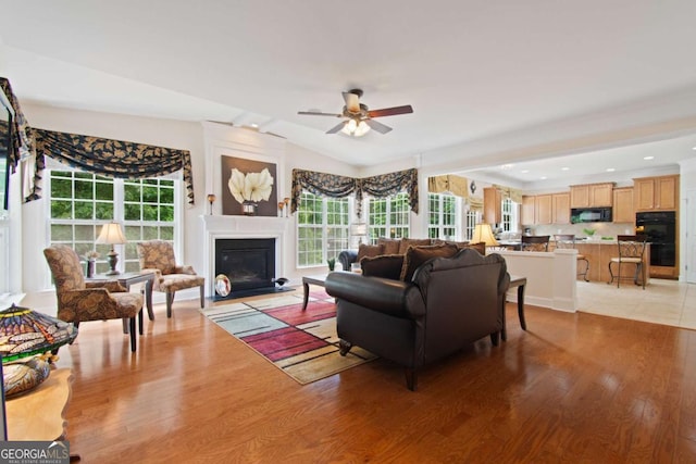 living area with light wood finished floors, ceiling fan, a glass covered fireplace, and lofted ceiling