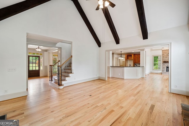 unfurnished living room with light wood finished floors, plenty of natural light, stairs, beam ceiling, and ceiling fan