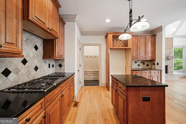 kitchen with stainless steel gas cooktop, crown molding, light wood finished floors, a center island, and backsplash