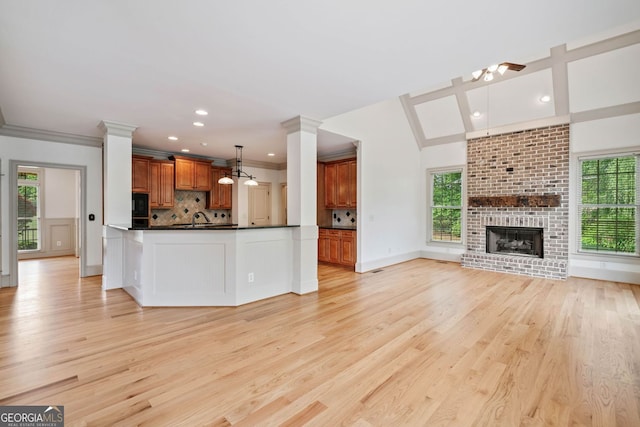 unfurnished living room featuring healthy amount of natural light, light wood-style flooring, ornate columns, recessed lighting, and crown molding