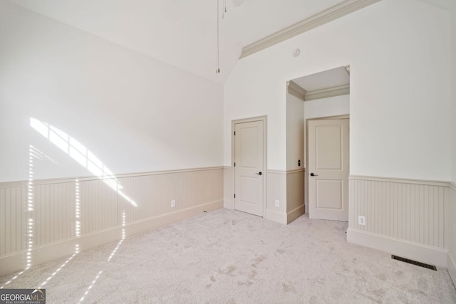 carpeted spare room featuring wainscoting, vaulted ceiling, and crown molding