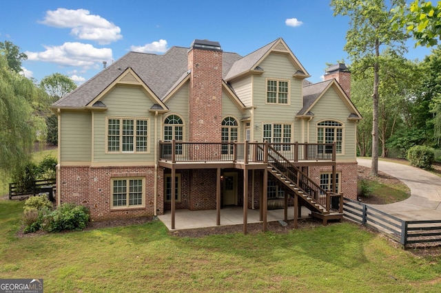 back of property featuring a chimney, brick siding, a patio, a deck, and a lawn