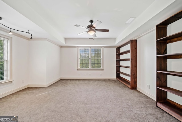 carpeted empty room featuring ceiling fan, baseboards, and a tray ceiling