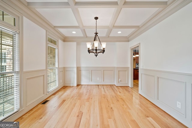 unfurnished dining area with a chandelier, beamed ceiling, light wood finished floors, coffered ceiling, and a decorative wall