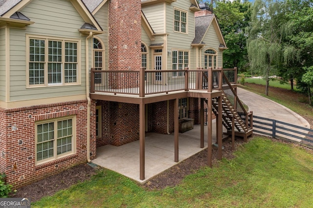 rear view of house featuring a patio, a wooden deck, brick siding, a chimney, and a shingled roof