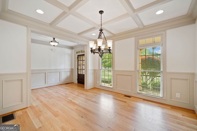 unfurnished dining area featuring coffered ceiling, a decorative wall, a chandelier, wainscoting, and beamed ceiling