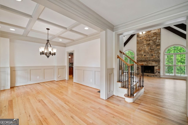 unfurnished dining area with a chandelier, beamed ceiling, wood finished floors, stairs, and a stone fireplace